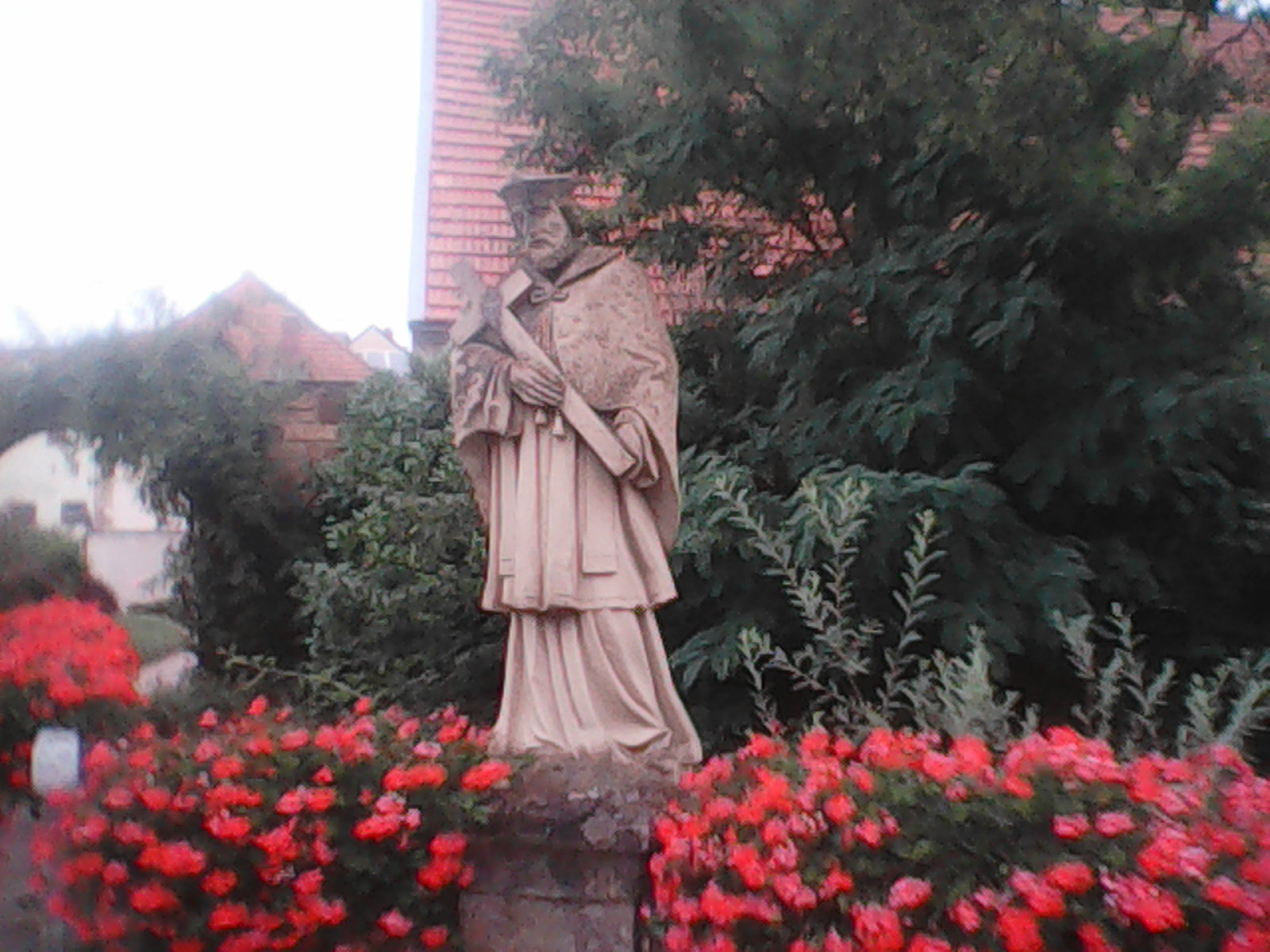 Statue of a holy man, surrounded by red flowers.